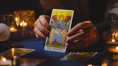 Close-Up-Of-Woman-Giving-Tarot-Card-Reading-On-Candlelit-Table-Holding-The-Lovers-Card-3